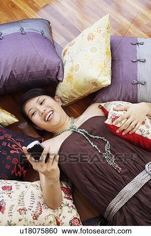 Stock Image - High angle view of a young woman smiling and operating a mobile phone. Fotosearch