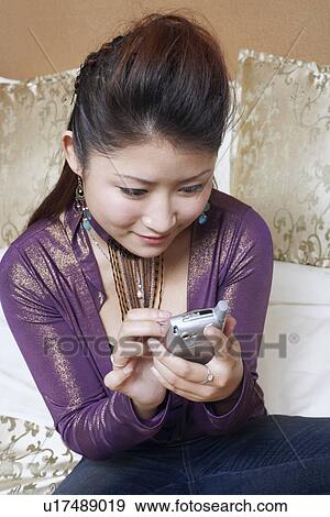 Stock Photo - High angle view of a young woman holding a mobile phone smiling. Fotosearch