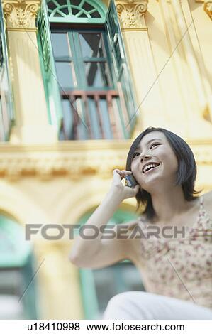 Stock Photo - Low angle view of a young woman talking on a mobile phone. Fotosearch