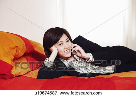 Portrait of a businesswoman lying on the bed and talking on a mobile phone View Large Photo Image Stock Photo - Portrait of a businesswoman lying on the bed and talking on a mobile phone. Fotosearch