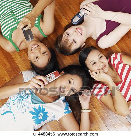 Stock Photograph - Portrait of four young women lying on a hardwood floor and holding mobile phones. Fotosearch