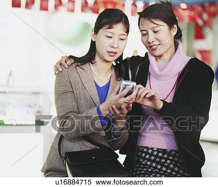 Two young women looking at a mobile phone View Large Photo Image Stock Photography - Two young women looking at a mobile phone. Fotosearch