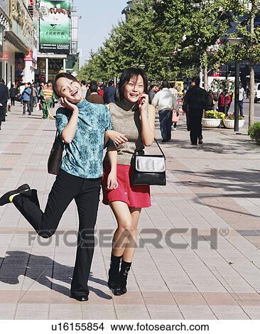 Picture - Two young women talking on mobile phones in a street. Fotosearch