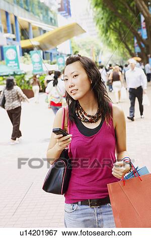 Young woman holding a mobile phone and carrying shopping bags View Large Photo Image Stock Photo - Young woman holding a mobile phone and carrying shopping bags. Fotosearch