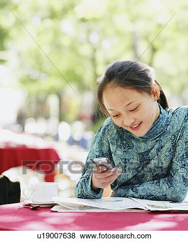 Young woman sitting in a restaurant and operating a mobile phone View Large Photo Image Stock Photo - Young woman sitting in a restaurant and operating a mobile phone. Fotosearch