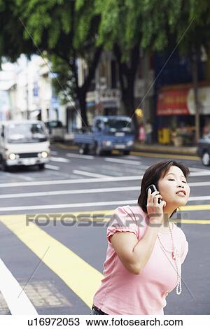 Stock Image - Young woman standing on the road and talking on a mobile phone. Fotosearch