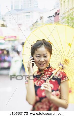 Young woman talking on a mobile phone holding a parasol View Large Photo Image Stock Image - Young woman talking on a mobile phone holding a parasol. Fotosearch