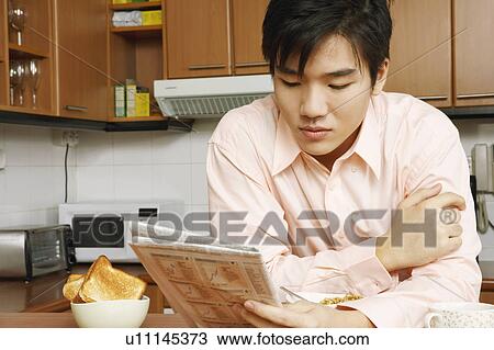 Close-up of a young man reading a newspaper at a kitchen counter View Large Photo Image Stock Image - Close-up of a young man reading a newspaper at a kitchen counter. Fotosearch