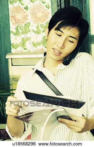 Close-up of a young man reading mail while talking on a cordless phone View Large Photo Image Stock Photograph - Close-up of a young man reading mail while talking on a cordless phone. Fotosearch