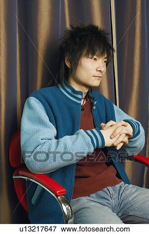 Close-up of a young man sitting on an armchair looking away View Large Photo Image Stock Photo - Close-up of a young man sitting on an armchair looking away. Fotosearch