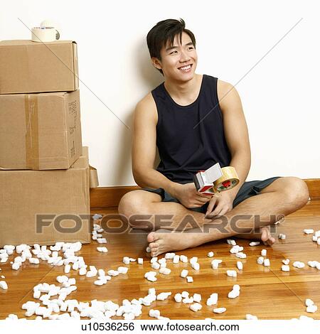 Stock Photograph - Close-up of a young man sitting on the floor and holding a tape dispenser. Fotosearch