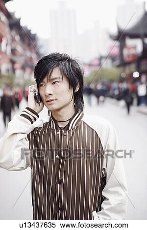 Stock Photography - Close-up of a young man using a mobile phone with his hands in his pockets. Fotosearch