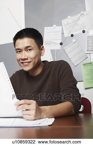 Stock Image - Portrait of a businessman holding a printout smiling. Fotosearch