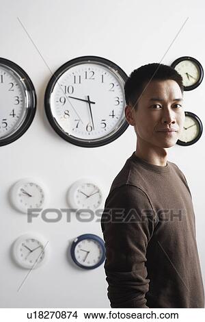 Picture - Portrait of a businessman standing in front of clocks on the wall. Fotosearch