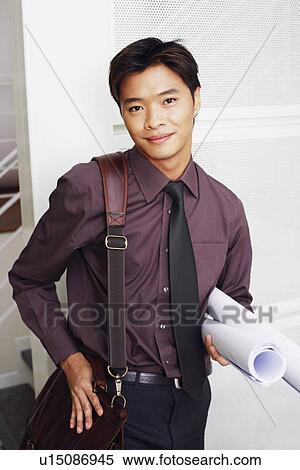 Stock Photography - Portrait of a male architect holding rolled up blueprints and smiling. Fotosearch