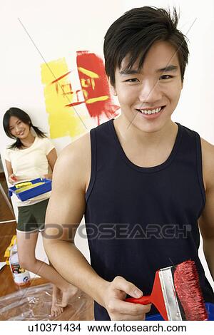 Portrait of a young man holding a paintbrush with a young woman standing in the background View Large Photo Image Picture - Portrait of a young man holding a paintbrush with a young woman standing in the background. Fotosearch