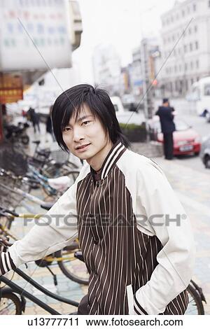 Stock Image - Portrait of a young man holding a bicycle. Fotosearch