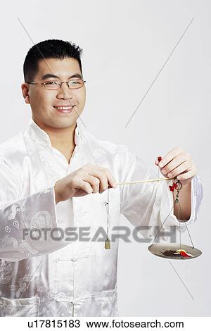 Stock Image - Portrait of a young man holding a balance scale. Fotosearch