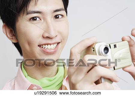 Stock Photograph - Portrait of a young man holding a digital camera. Fotosearch