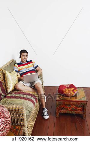 Stock Image - Portrait of a young man listening to music and using a laptop. Fotosearch