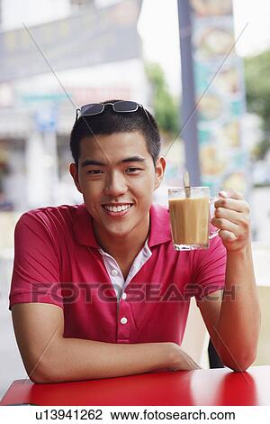 Stock Image - Portrait of a young man sitting in a cafe and holding a mug of coffee. Fotosearch