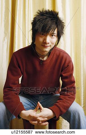 Stock Photo - Portrait of a young man sitting on a stool with his hands clasped. Fotosearch