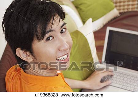 Stock Photo - Portrait of a young man smiling and using a laptop. Fotosearch