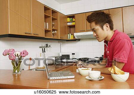 Side profile of a young man looking at a laptop at a kitchen counter View Large Photo Image Stock Photography - Side profile of a young man looking at a laptop at a kitchen counter. Fotosearch