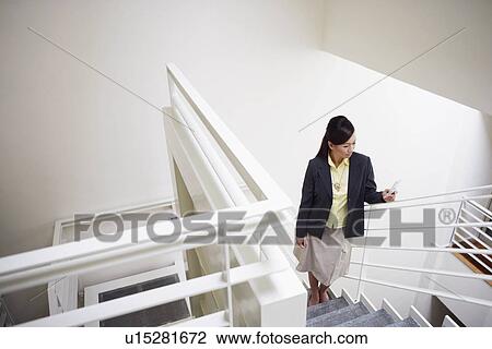 High angle view of a young woman standing on a staircase and holding a mobile phone View Large Photo Image Stock Image - High angle view of a young woman standing on a staircase and holding a mobile phone. Fotosearch