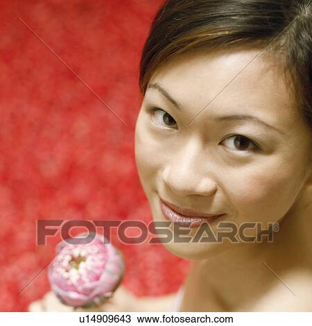 Stock Image - Portrait of a young woman holding a flower and smiling. Fotosearch