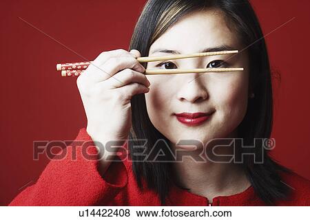 Stock Photo - Portrait of a young woman looking through chopsticks. Fotosearch