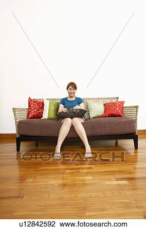 Stock Image - Portrait of a young woman sitting on a couch and smiling. Fotosearch