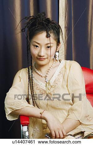 Stock Image - Portrait of a young woman sitting on a chair smiling. Fotosearch