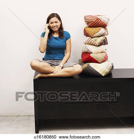 Stock Image - Young woman sitting on a cabinet and talking on a mobile phone. Fotosearch