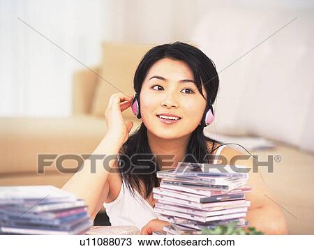 Stock Image - Closed Up Image of a Young Adult Woman Listening to Some Music, Looking Sideways, Some CDs in the Front, Front View, Differential Focus. Fotosearch