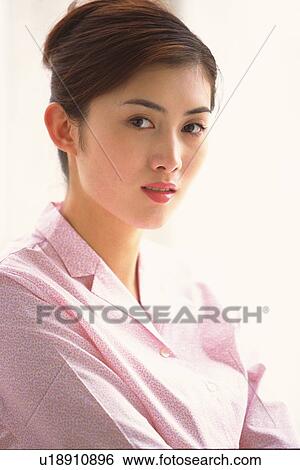 Stock Photograph - Closed Up Image of a Young Adult Woman In Front of a White Wall, Wearing a Pink Blouse, Side View, Looking at Camera. Fotosearch