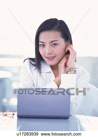 Stock Photo - Image of a Business Woman Sitting In Front of a Laptop, Posing, Looking at Camera, Smiling, Front View. Fotosearch