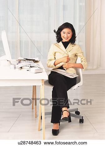 Stock Image - Image of a Businesswoman at her Desk, Sitting on a Chair, Smiling, Front View. Fotosearch
