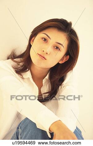 Stock Photo - Image of a Mid Adult Woman Sitting In Front of a White Wall, Posing, Looking at Camera, Front View. Fotosearch