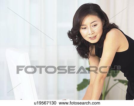 Stock Image - Image of a Mid Adult Woman Standing Next to her Laptop, Side View, Smiling, Looking Down. Fotosearch