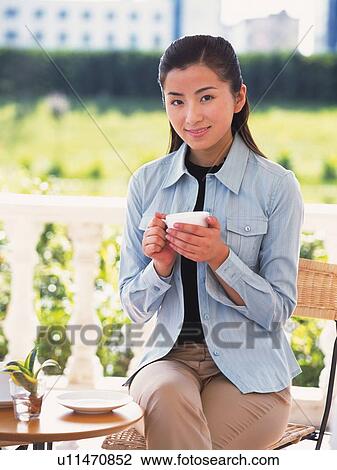 Image of a Young Adult Woman Drinking a Cup of Coffee Outside While Sitting, Looking at Camera, Smiling, Differential Focus View Large Photo Image Stock Image - Image of a Young Adult Woman Drinking a Cup of Coffee Outside While Sitting, Looking at Camera, Smiling, Differential Focus. Fotosearch