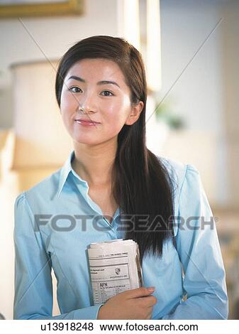 Stock Photo - Image of a Young Adult Woman Indoors, Holding a Newspaper, Smiling and Looking at Camera, Front View, Differential Focus. Fotosearch