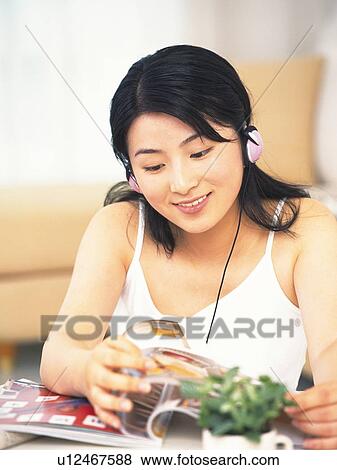 Stock Photo - Image of a Young Adult Woman Listening to Some Music While Reading a Magazine, Smiling, Looking Down, Front View, Differential Focus. Fotosearch