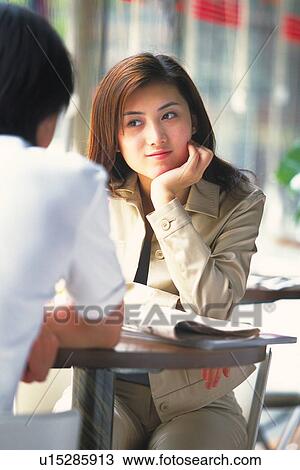 Stock Image - Image of a Young Adult Woman Sitting at a Table With a Man, Front View, Rear View, Differential Focus. Fotosearch