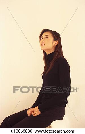Stock Image - Image of a Young Adult Woman Sitting In Front of a White Wall Looking Up, Smiling, Side View. Fotosearch
