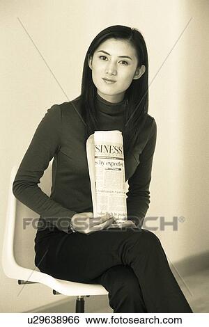 Stock Photograph - Image of a Young Adult Woman Sitting on a Chair, Holding a Newspaper, Looking at Camera, Front View. Fotosearch