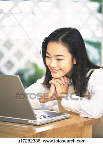 Stock Photograph - Image of a Young Adult Woman Smiling at her Laptop, Side View, Differential Focus. Fotosearch