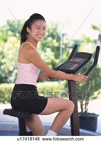 Stock Photo - Image of a Young Adult Woman, Exercising on a Bicycle, Smiling, Looking at Camera, Side View, Differential Focus. Fotosearch