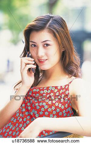 Stock Photo - Image of a Young Adult woman Taking on a Cell Phone, Wearing a Red Dress, Smiling, Side View, Looking at Camera. Fotosearch