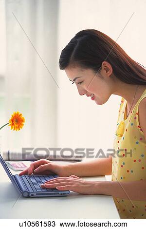 Image of a Young Adult Woman Using a Computer, Next to a Little Orange Flower, Smiling, Side View View Large Photo Image Stock Image - Image of a Young Adult Woman Using a Computer, Next to a Little Orange Flower, Smiling, Side View. Fotosearch
